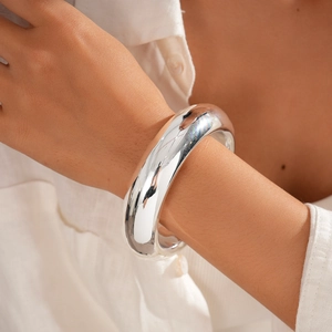 Close-up of a wide polished silver cuff bracelet on wrist over a white linen shirt background