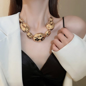 Close-up of a chunky gold statement necklace with irregular links on a female model