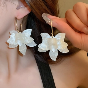 Detail of pearlescent white resin flower earrings with elegant gold hooks on model