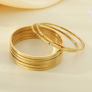 Gros plan de bracelets joncs empilés en acier doré 18K sur un fond en soie beige