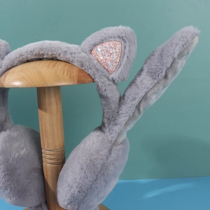Detail of grey plush earmuffs with pink sequin cat ears on a wooden stand