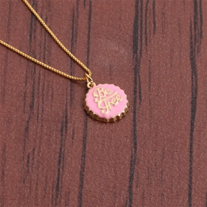 Close-up of a pink bottle cap pendant with gold Be Free text on a 18K gold plated chain