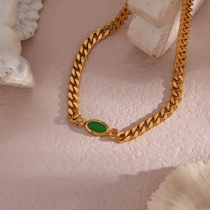 Macro detail of 18K gold-plated Cuban chain necklace with green oval gemstone inlay