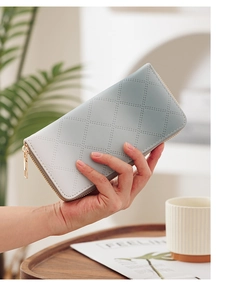Detail of grey-blue quilted faux leather long wallet with elegant gold zipper held by model