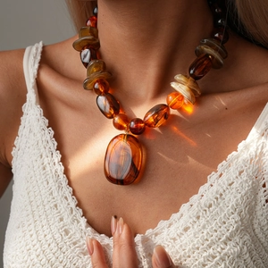 Detail of amber acrylic irregular bead necklace with oval pendant on model's neck