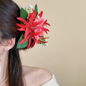 Detailed view of a large layered red floral hair clip with green leaves worn on a model