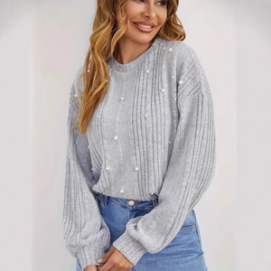 Détail d'un pull gris en maille avec manches lanternes et perles blanches élégantes