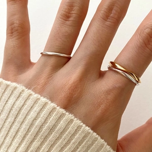 Detailed view of silver and gold minimalist twisted rings worn on hand with knit sleeve