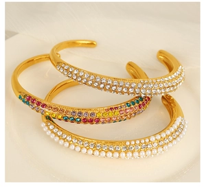 Detailed view of gold C-shaped open bracelets with white pearls and sparkling zircons