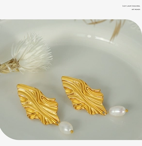 Detailed view of golden leaf earrings with elegant white pearls on a minimalist ceramic plate