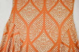 Detailed view of orange dress fabric with white geometric diamond patterns and smooth texture