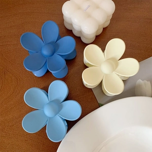 Three matte flower claw clips in blue and yellow colors on a wooden background