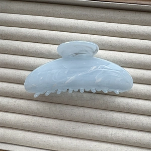 Detail of light blue marble textured hair claw clip on beige velvet display