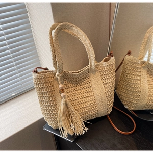 Detail of a beige woven straw tote bag featuring decorative tassels and natural textures