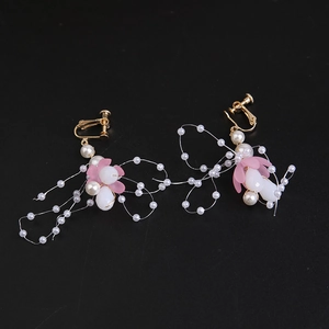 Detail view of golden leaf earrings with pink petals and white pearls on black background