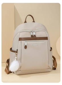Close-up of beige waterproof nylon backpack featuring brown trim and pearl fur ball charm