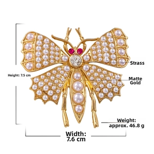 Detailed view of vintage matte gold butterfly brooch with pearls, rhinestones and red gems