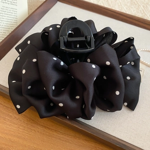 Detail of black polka dot fabric hair claw clip with strong metal spring on a wooden tray