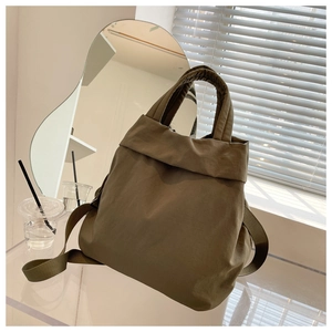 Detailed shot of olive green nylon handbag featuring reinforced straps on a modern glass table
