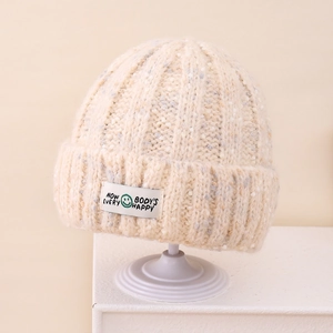 Detail of light beige knit beanie with colorful flecks and a smiley face woven patch