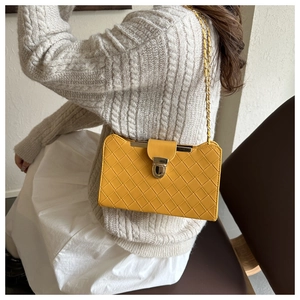 Detail of yellow woven shoulder bag featuring a gold metal lock and chain strap on a model