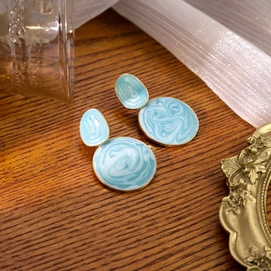 Detail of light blue marble drip oil earrings with gold edges on a wooden background