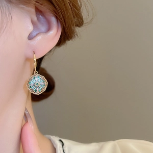 Detail of vintage gold flower earring with green zircon worn on a model ear