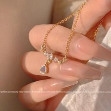 Detail of gold butterfly necklace with blue opal drop pendant held in hand close-up