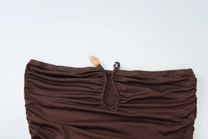 Detail of ruched brown fabric featuring a silver metallic bead and orange stone buckle