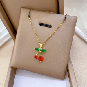 Close-up of luxury cherry pendant with red crystals and green leaf on gold chain