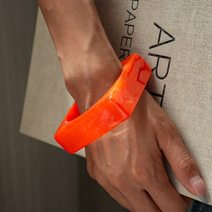Close-up of a bright orange acrylic geometric bangle with artistic marbled texture