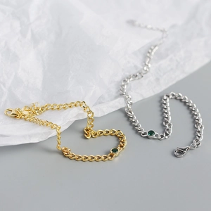 Close-up of gold and silver chunky curb chain bracelets featuring green gemstone charms