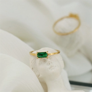 Artistic detail of an 18K gold-plated ring featuring a rectangular green emerald gemstone