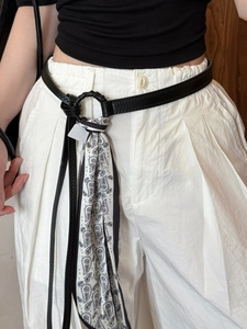 Detail of a thin black leather belt with black and white paisley silk scarf decoration