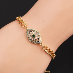Gold plated evil eye bracelet with green blue zircons worn on wrist over black background