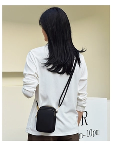 Rear view of a black canvas crossbody phone bag with gold zippers and adjustable strap