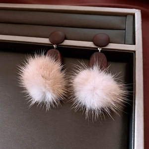Macro detail of beige fluffy pom-pom drop earrings on a gray jewelry display tray