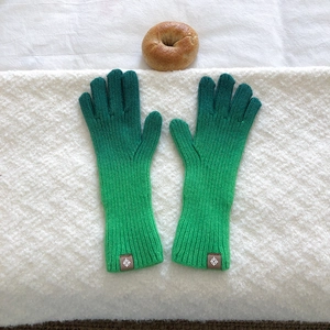 Detail of gradient green knit gloves with extended ribbed cuffs on white textile surface