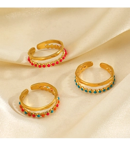 Detail of three gold adjustable rings with colorful enamel dots on beige satin