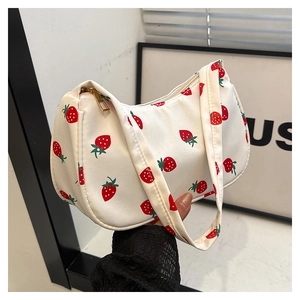 Close-up of white canvas underarm bag featuring vibrant red strawberry print and gold zipper