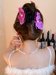 Detail of purple orchid flower hair clips on model's updo hairstyle with pearl necklace