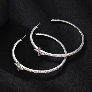 Sparkling silver hoop earrings with zircon pavé and delicate cross charm on black background