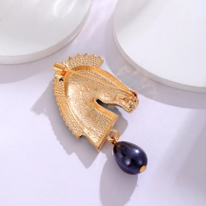 Golden zebra horse head brooch with navy blue pearl pendant on a textured metal surface