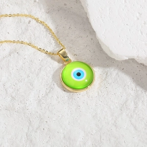 Gold evil eye pendant necklace with green resin disc and dainty chain on white stone