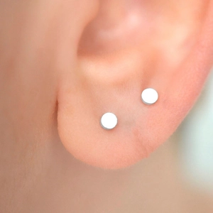 Minimalist silver titanium steel round stud earrings shown worn on a model's earlobe
