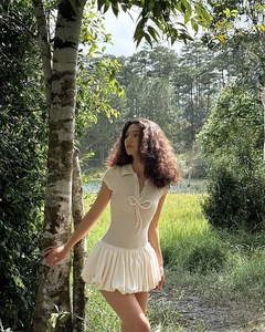 Detail eines cremefarbenen Strickkleides mit Schleife und ausgestelltem Rock im Wald