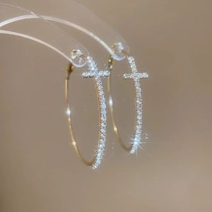 Gros plan sur des créoles dorées ornées d'un pendentif en croix serti de diamants