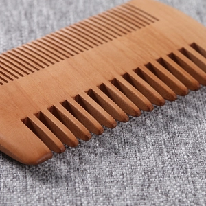 Double-sided peach wood comb with fine and wide teeth on a grey fabric background