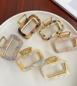 Close-up of six acetate hair claws in various patterns arranged in a white circular tray