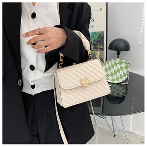 Detail of white pleated handbag featuring a gold chain and heart-shaped metal buckle